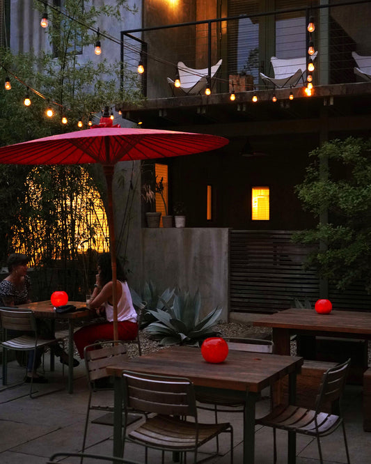Outdoor patio with red umbrella, tables, and chairs under string lights.
