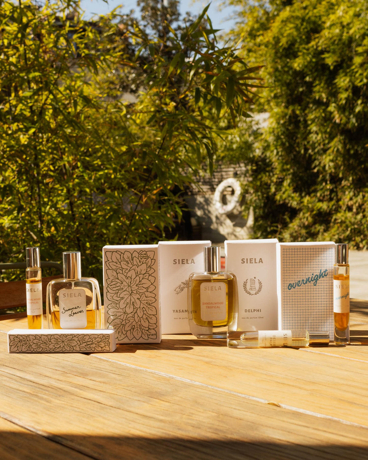 Collection of Siela perfume bottles and packaging on a wooden surface with a blurred natural background