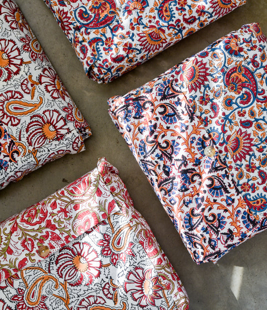 Four folded reversible duvet covers with a floral pattern featuring a mix of orange, red, and blue colors on a white background sitting on top of concrete surface.