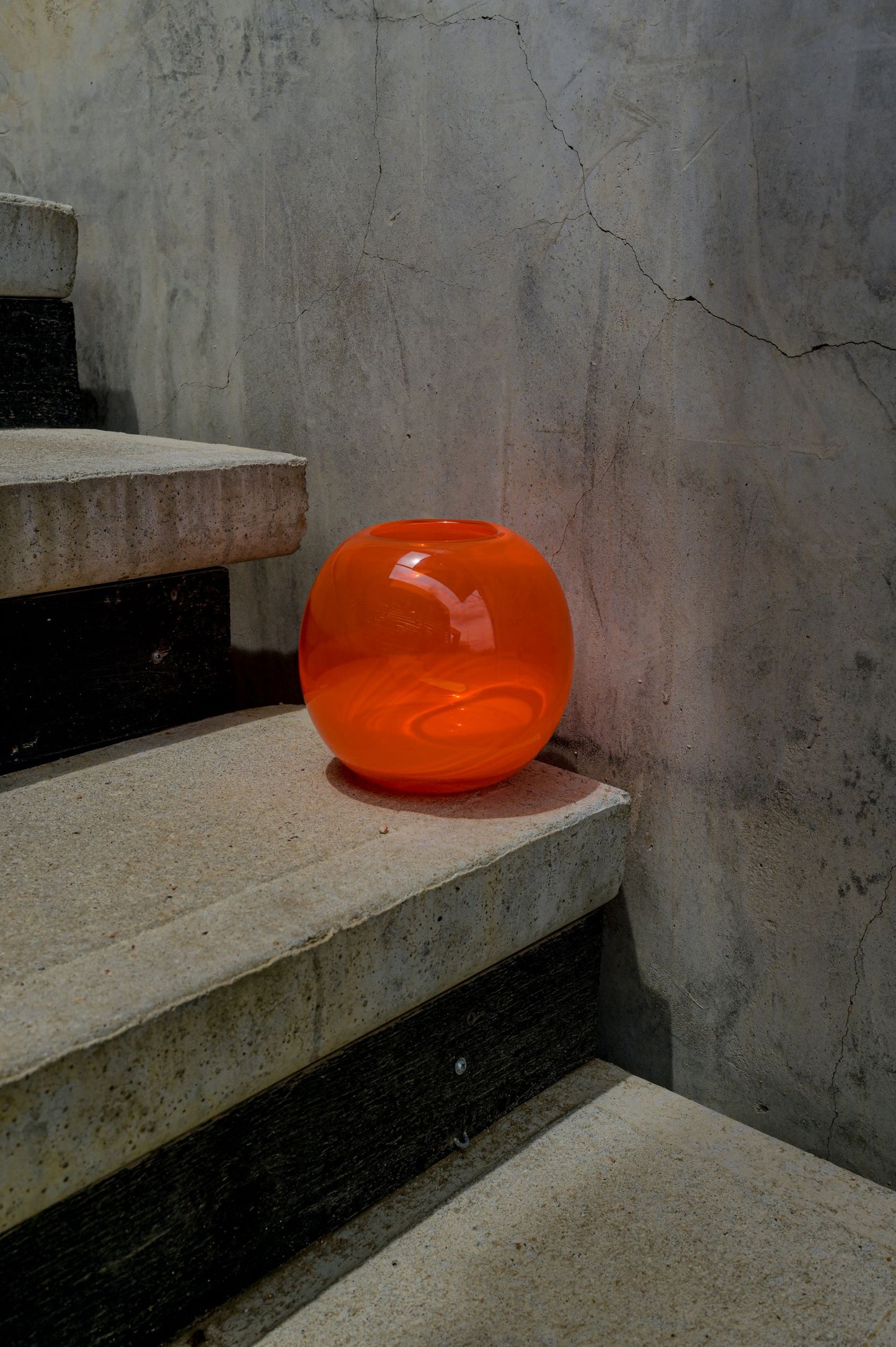 A red globe-shaped glass candle holder sitting on concrete stairs in moody lighting