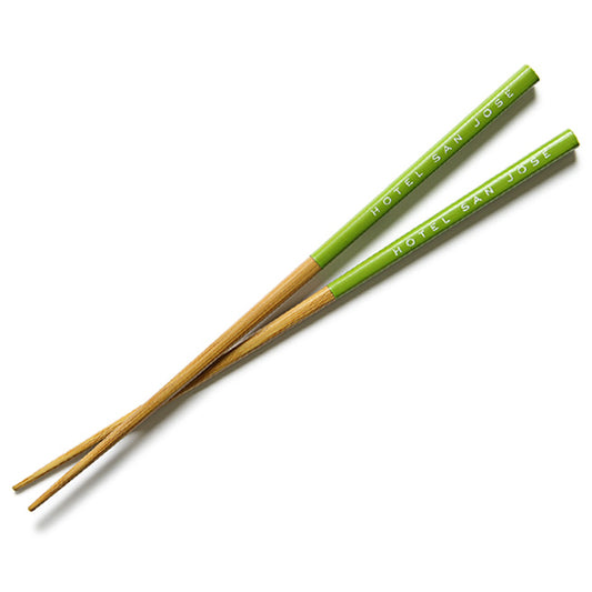 A pair of chopsticks with 'Hotel San Jose' text printed along the sides, predominantly green with beige accents.