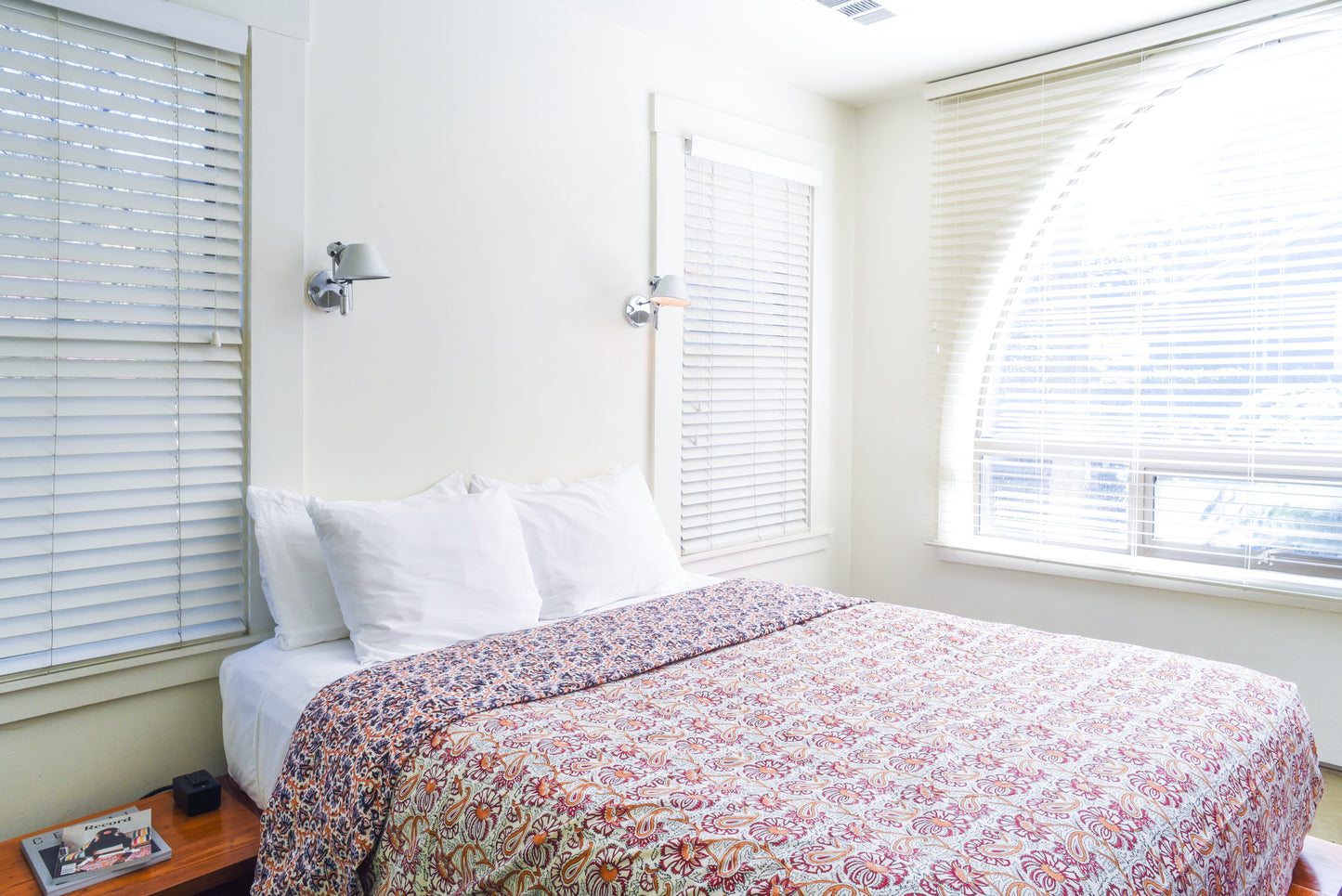 Room inside hotel san jose featuring a queen sized bed with floral duvet surrounded by bright windows