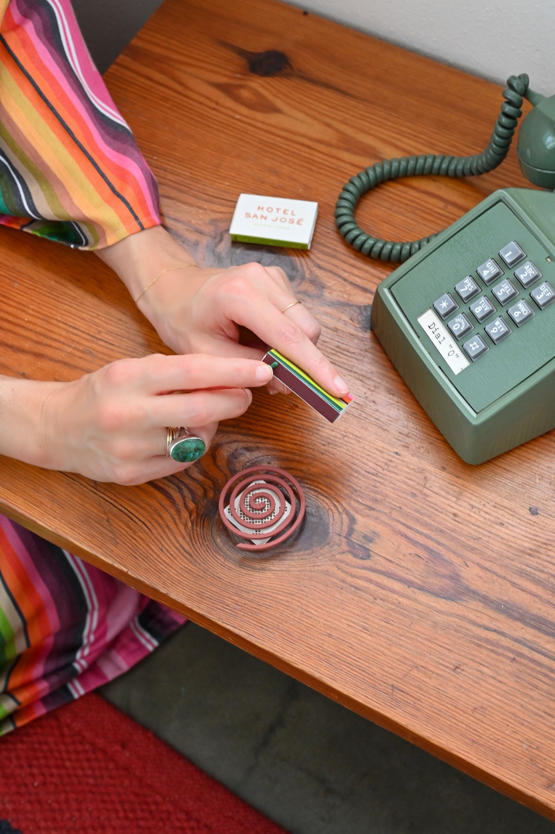 A photograph of a hands wearing a pink striped robe lighting a coiled incense sitting on top of wooden table 