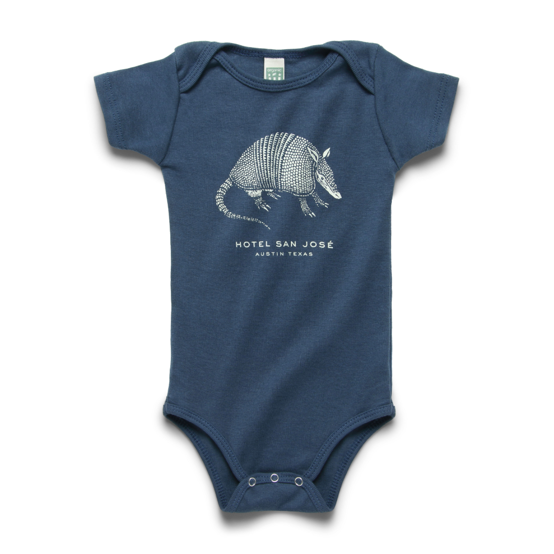 A blue short-sleeved baby onesie with a illustrated print of an armadillo and the text 'HOTEL SAN JOSE'.