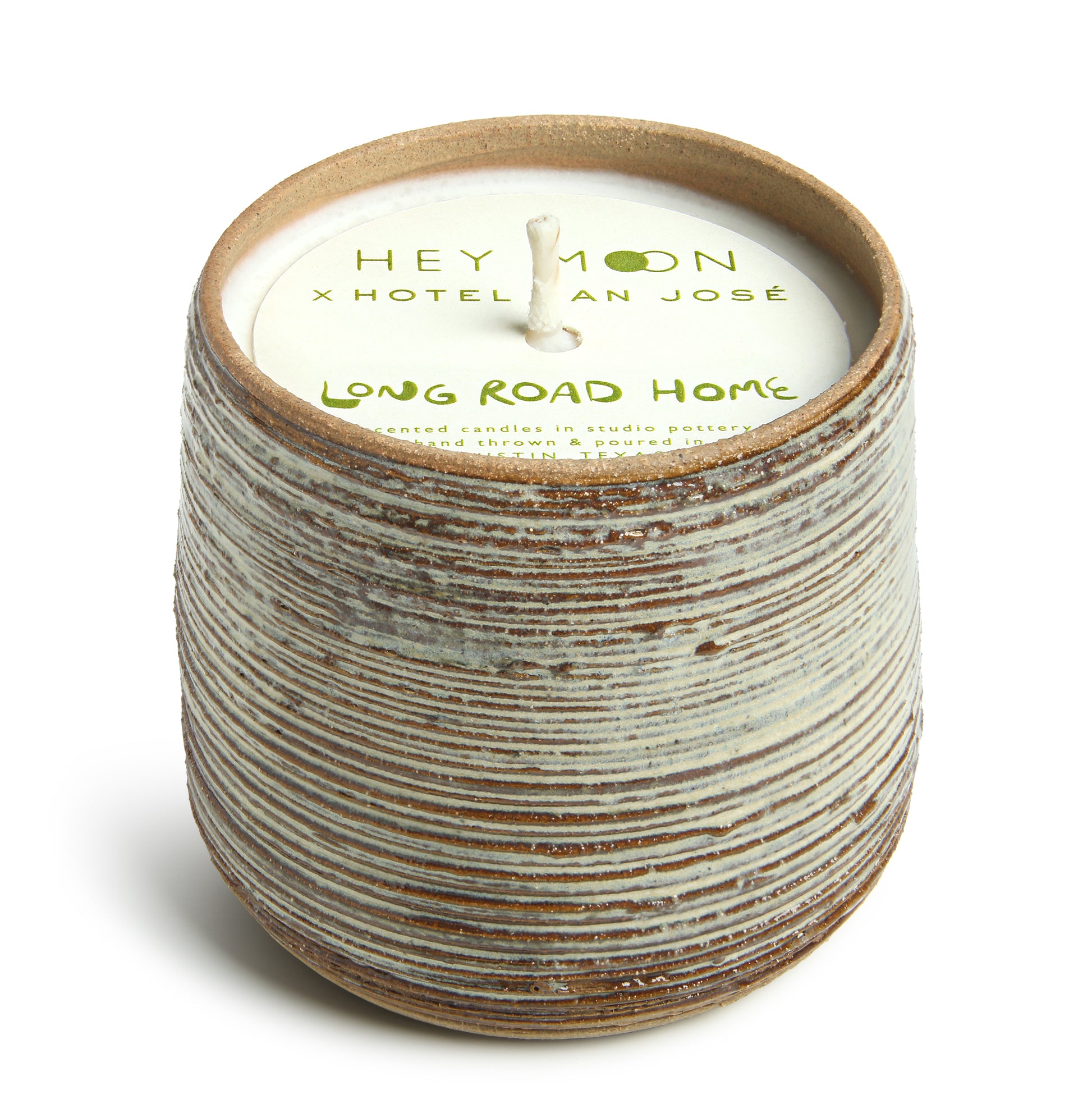 A cylindrical ceramic candle vessel with a striped pattern, including paper topper branded with 'Hey Moon x Hotel San Jose' and the name 'Long Road Home'.