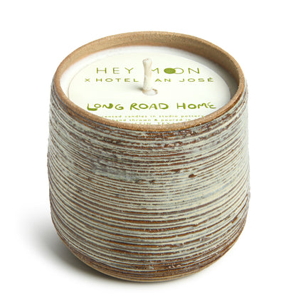 A cylindrical ceramic candle vessel with a striped pattern, including paper topper branded with 'Hey Moon x Hotel San Jose' and the name 'Long Road Home'.