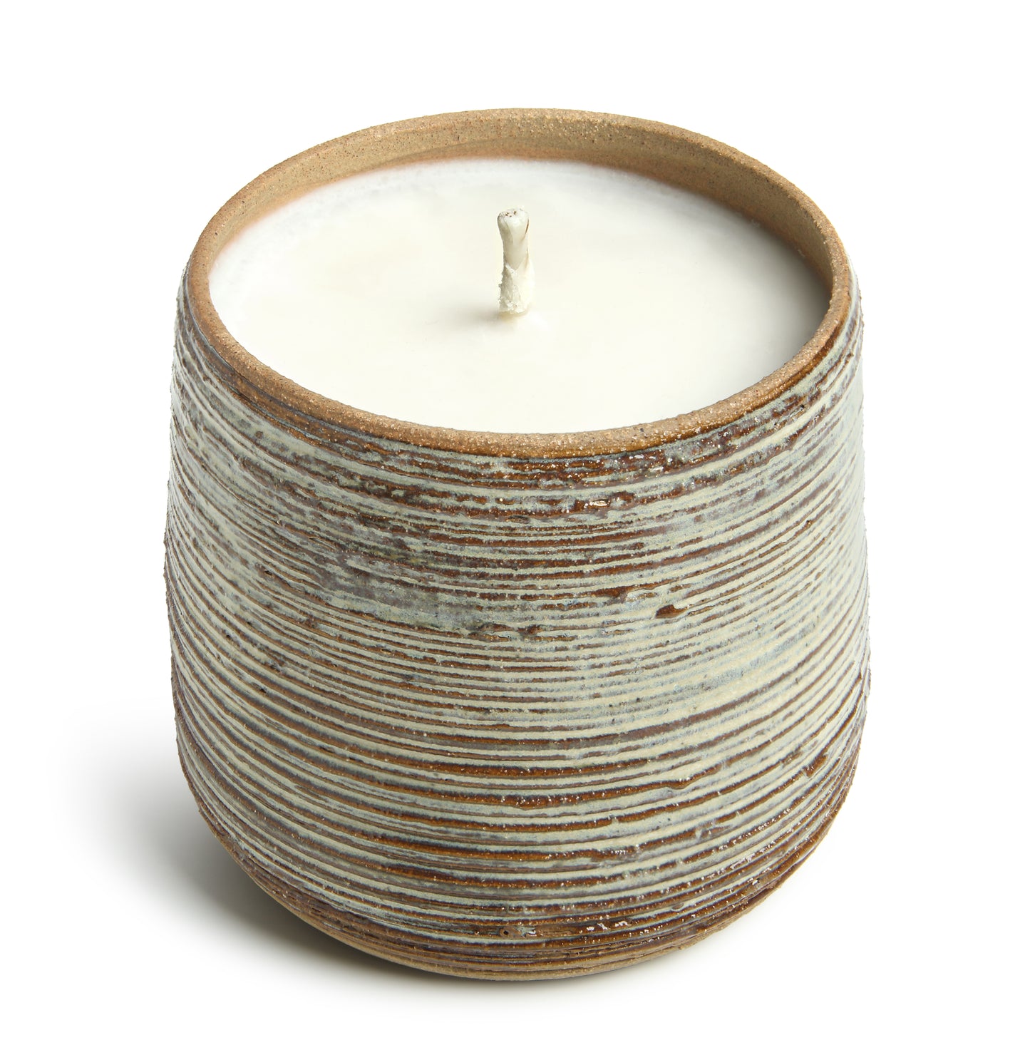 A candle in a cylindrical handmade ceramic vessel with a striped pattern.