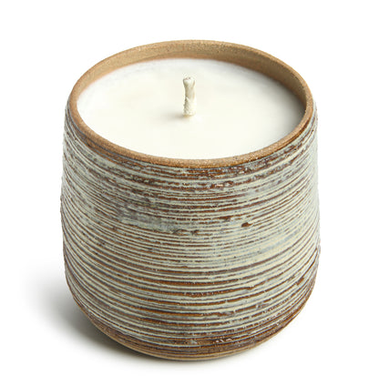 A candle in a cylindrical handmade ceramic vessel with a striped pattern.