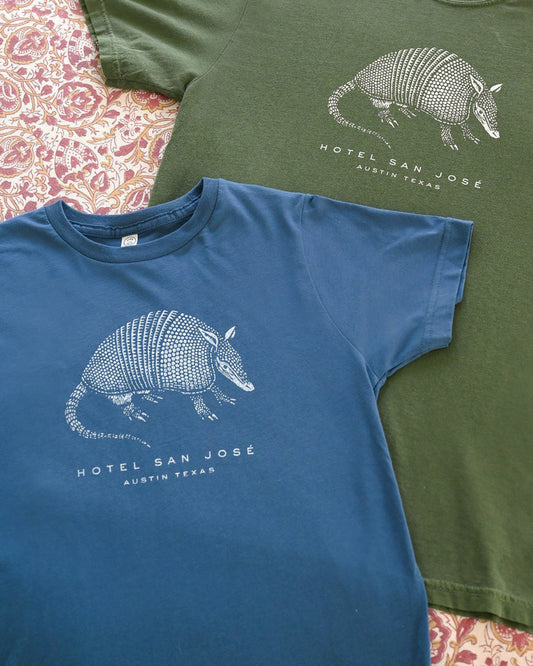 Two t-shirts, one blue and one green, with armadillo graphics and text on a patterned surface.