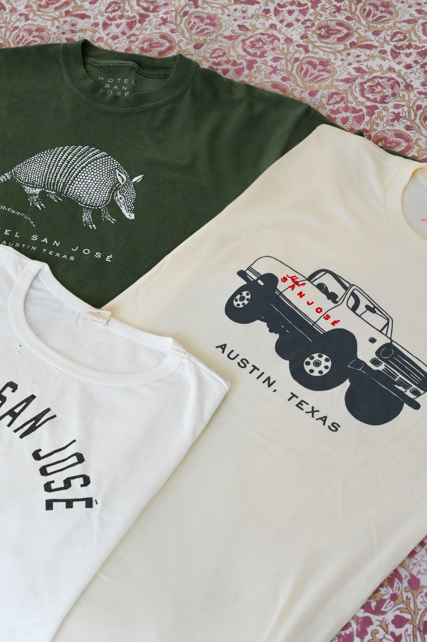 Three t-shirts with different designs on a patterned surface, all reading 'HOTEL SAN JOSE AUSTIN TEXAS'
