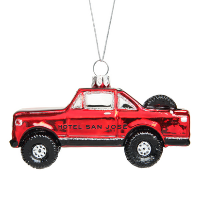 A red glass ornament in the shape of a vintage truck with 'HOTEL SAN JOSE' written on the side. The ornament is adorned with glitter and has a loop for hanging.