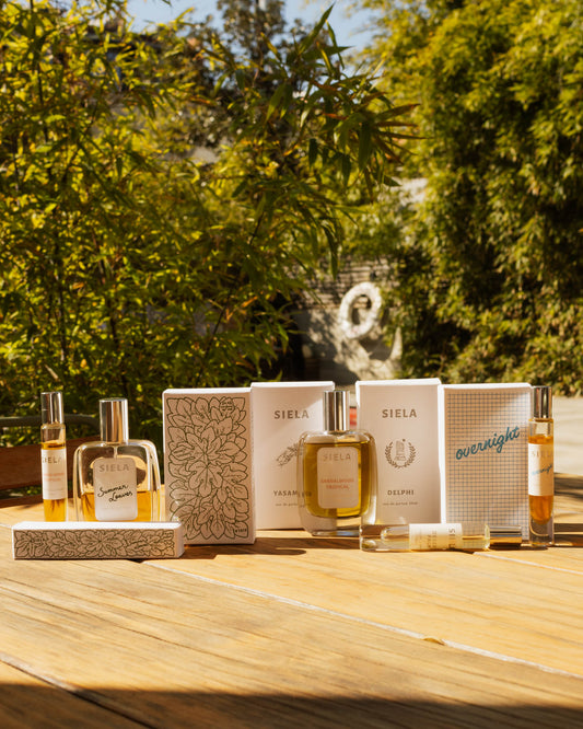 Collection of Siela perfume bottles and packaging on a wooden surface with a blurred natural background