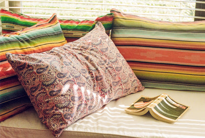 Colorful striped cushions and a patterned pillow on a sofa with a window in the background.