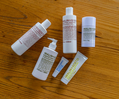 Photograph of malin and goetz apothecary products laying on top of wooden table.