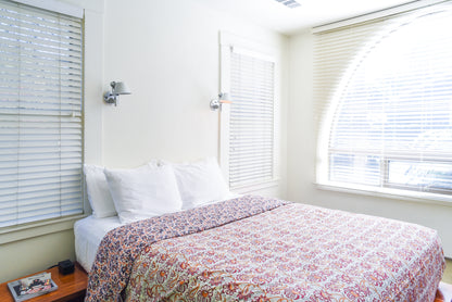 Room inside hotel san hose featuring queen size bed with floral duvet cover surrounded by windows.